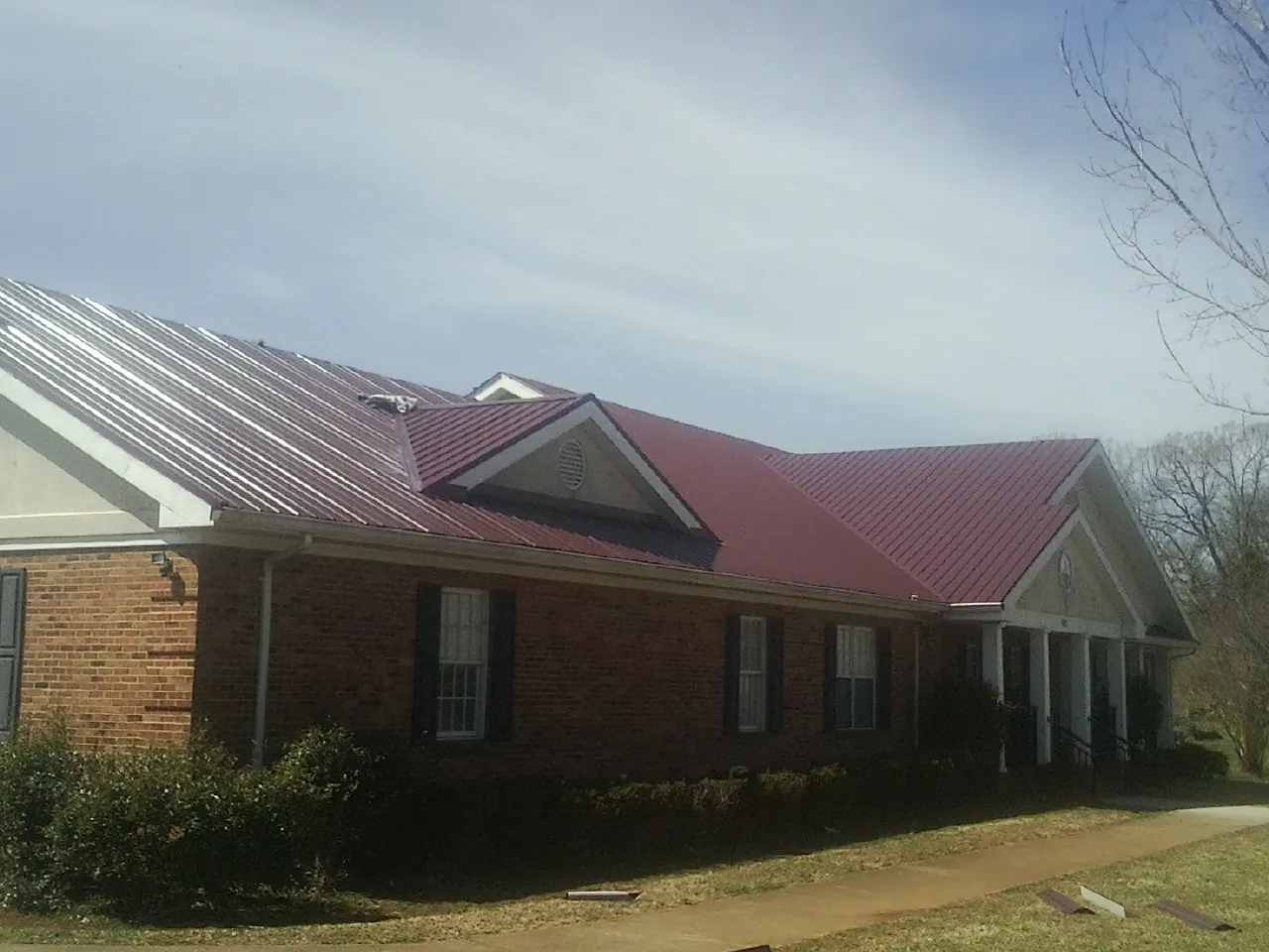 Red metal roof with gabled entries on a long brick building, from a Hail Damage Roof Repair job in Sullivan